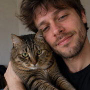 Ein Mann hält eine getigerte Katze im Arm und lehnt seinen Kopf an sie.