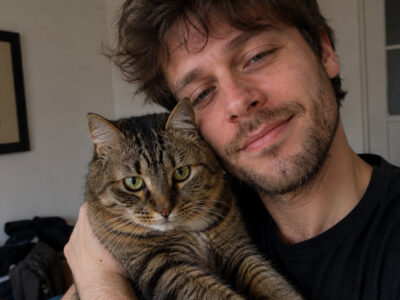 Ein Mann hält eine getigerte Katze im Arm und lehnt seinen Kopf an sie.