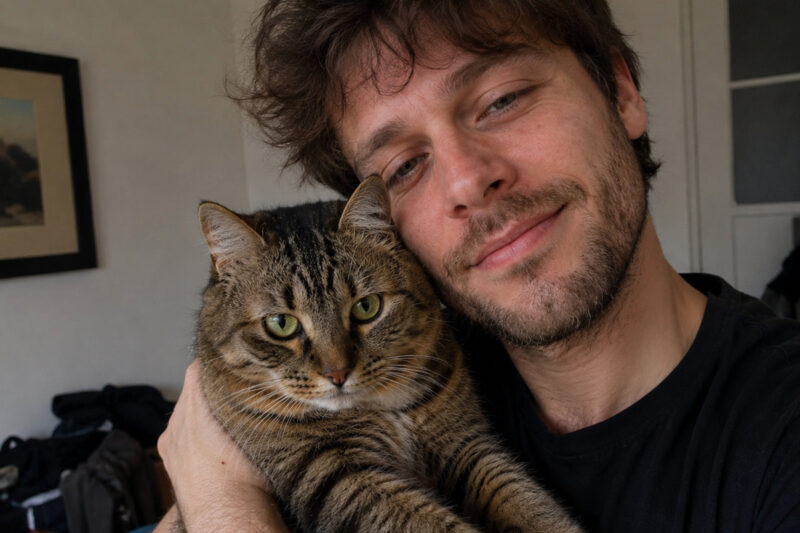 Ein Mann hält eine getigerte Katze im Arm und lehnt seinen Kopf an sie.