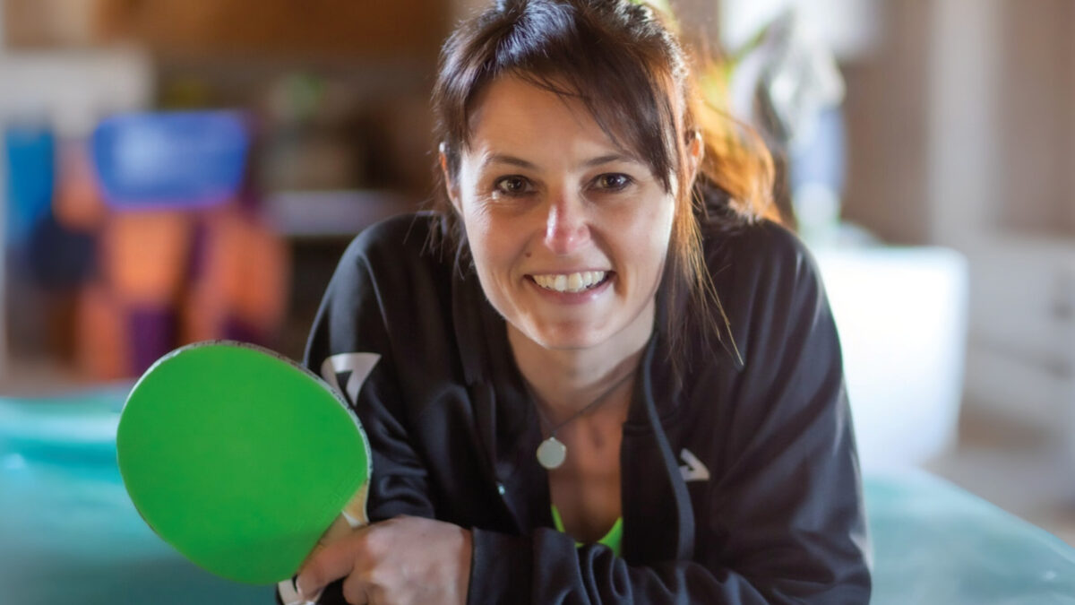 Anke Leidenberger lächelt in die Kamera und hält einen grünen Tischtennisschläger in der Hand.