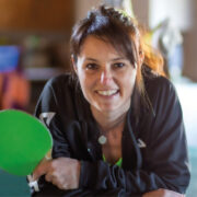 Anke Leidenberger lächelt in die Kamera und hält einen grünen Tischtennisschläger in der Hand.