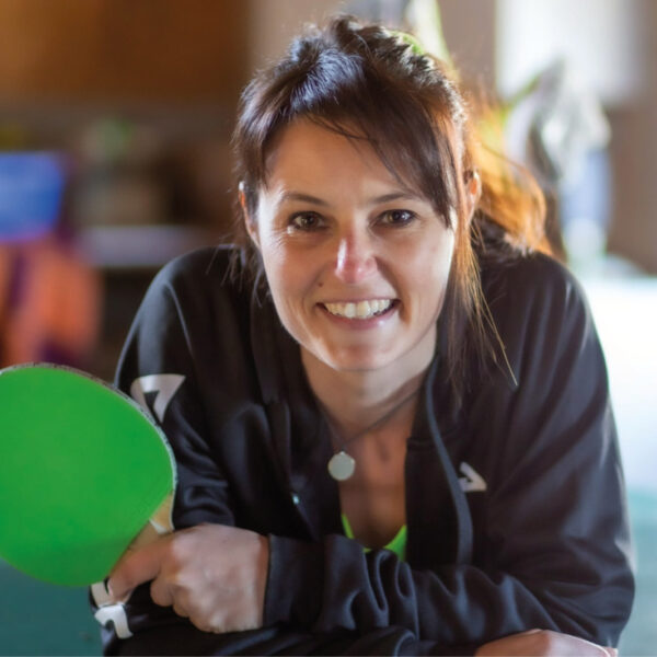 Anke Leidenberger lächelt in die Kamera und hält einen grünen Tischtennisschläger in der Hand.