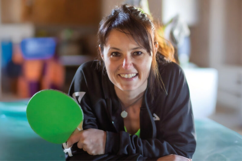 Anke Leidenberger lächelt in die Kamera und hält einen grünen Tischtennisschläger in der Hand.
