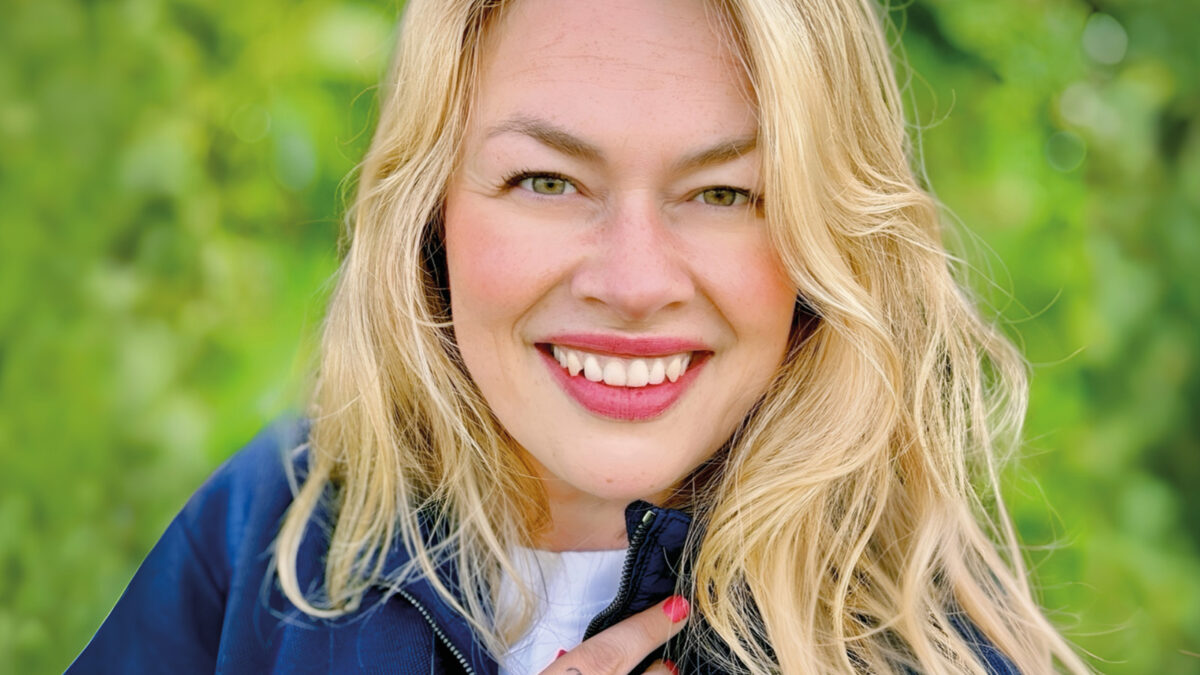 Porträt einer lächelnden blonden Frau (Nadine), die von chronischem Clusterkopfschmerz betroffen ist.