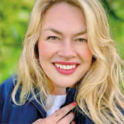 Porträt einer lächelnden blonden Frau (Nadine), die von chronischem Clusterkopfschmerz betroffen ist.