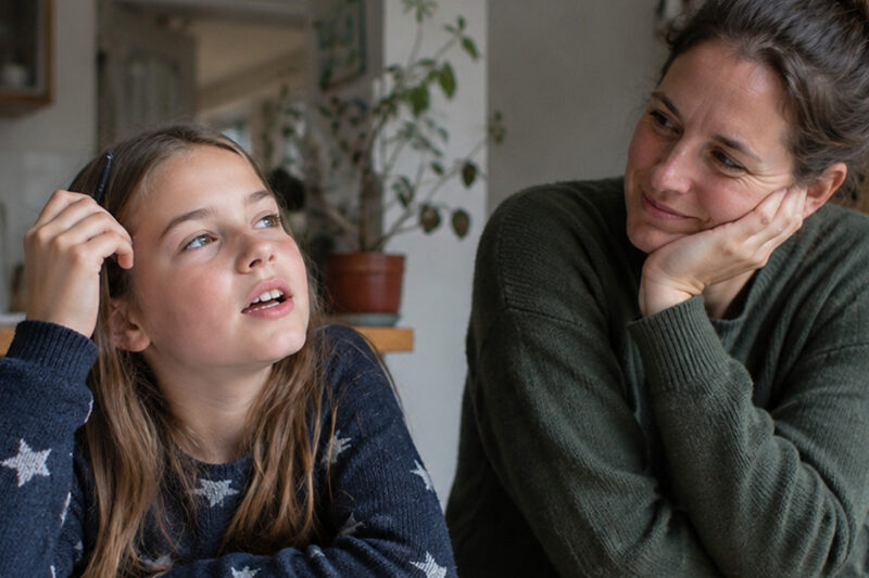 Mutter und Tochter sitzen gemeinsam am Tisch und sprechen miteinander