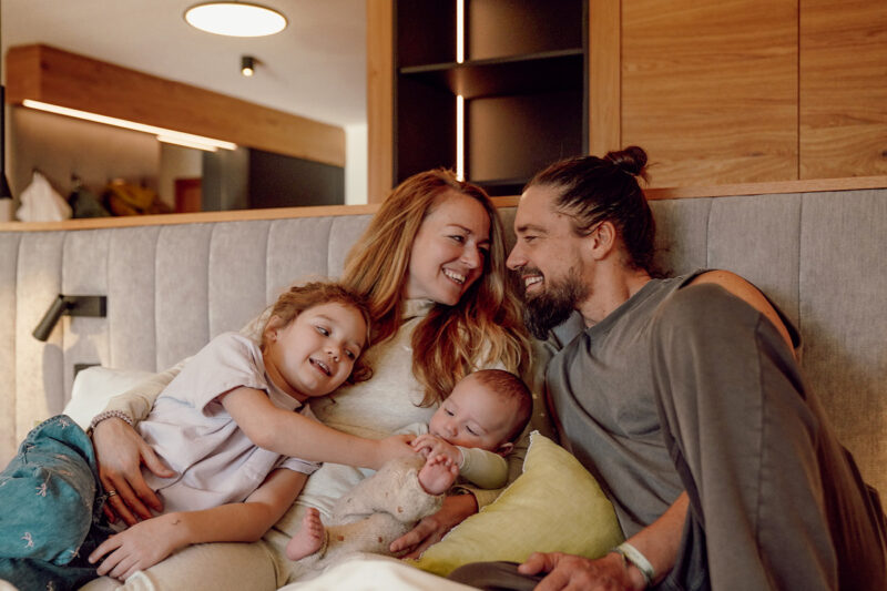 Familie mit zwei Kindern entspannt gemeinsam auf einem Bett in der Ferienwelt Kesselgrub