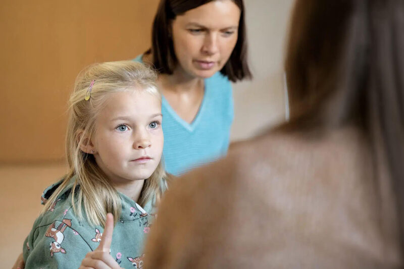 Mädchen in einer Gesprächssituation mit einer erwachsenen Frau im Hintergrund